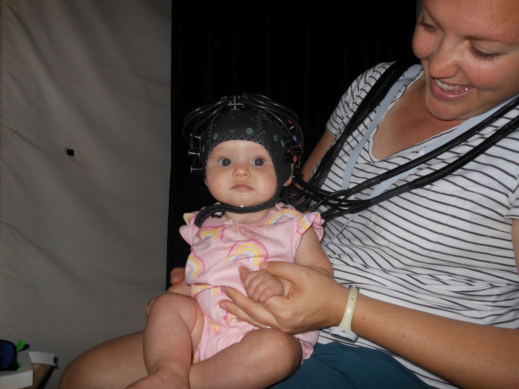 Infant in a neuroimaging headcap, seated on mother's lap.